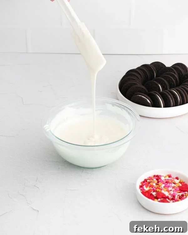 white chocolate being drizzled from a spatula into a bowl of melted white chocolate