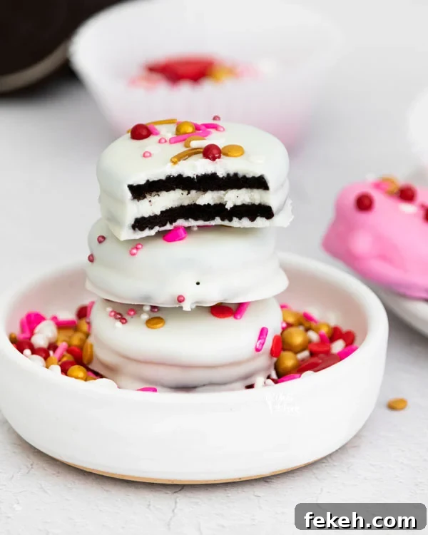 3 Valentine's Chocolate Covered Oreos stacked in a small white bowl filled with sprinkles with a bite mark in the top Oreo