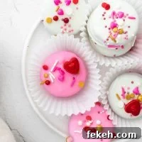 overhead shot of pink and white Valentine's Chocolate Covered Oreos in white paper holders on a white plate