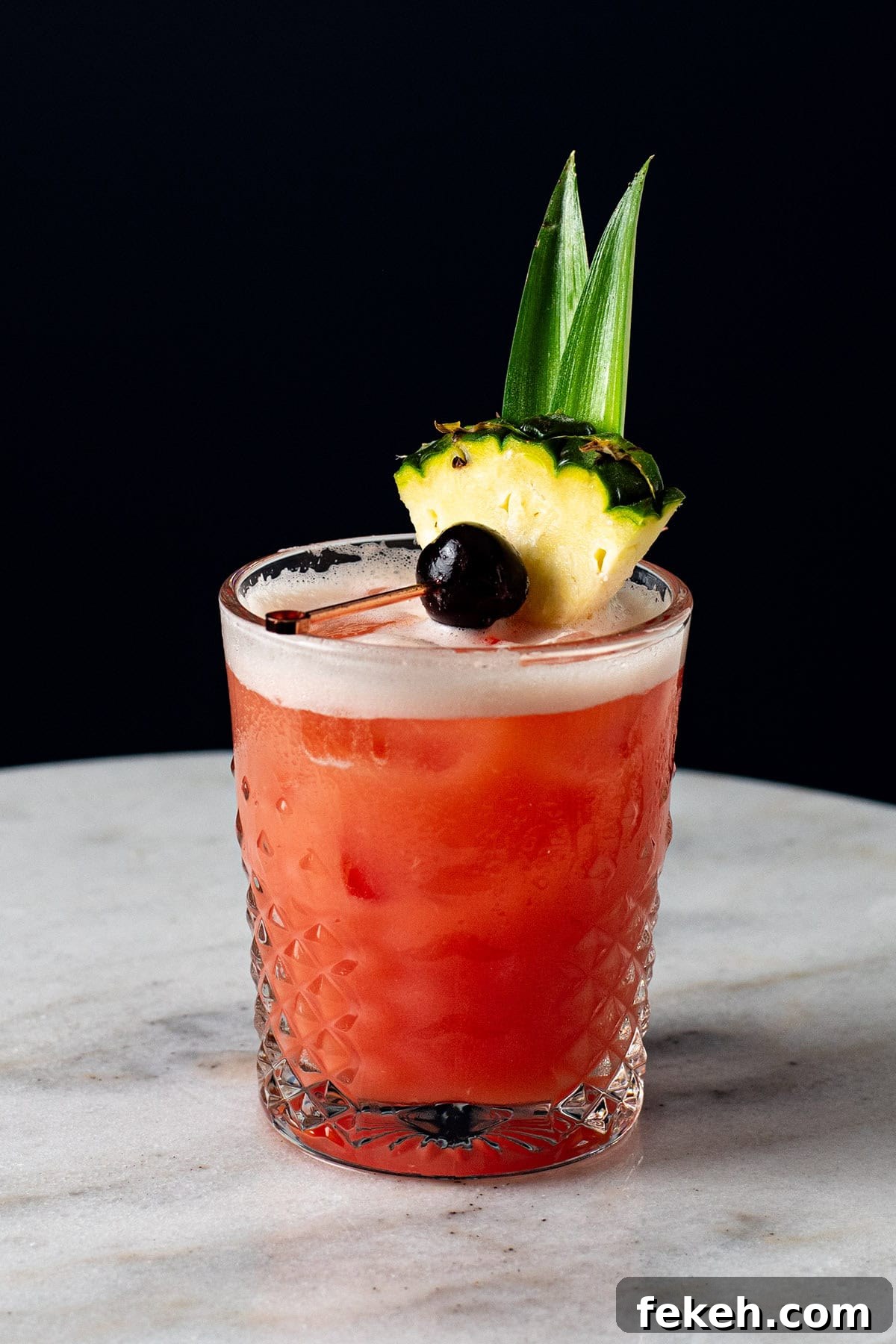 A red-hued Jungle Bird cocktail garnished with a pineapple wedge, pineapple frond, and a brandied cherry.