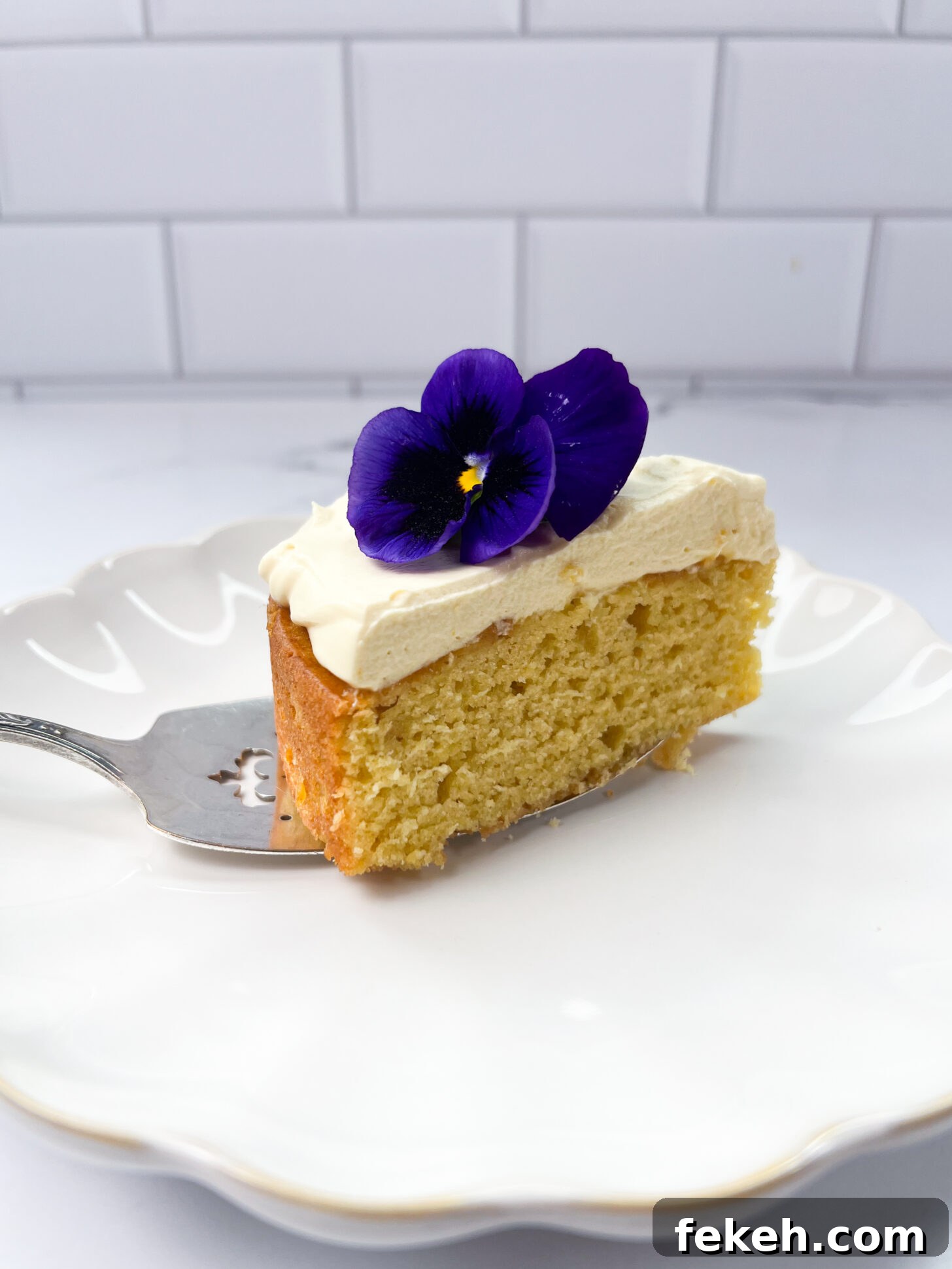 Mango Cake with Mascarpone Whipped Cream Frosting 6 A slice of mango cake with mango mascarpone whipped cream frosting, topped with a pansy.