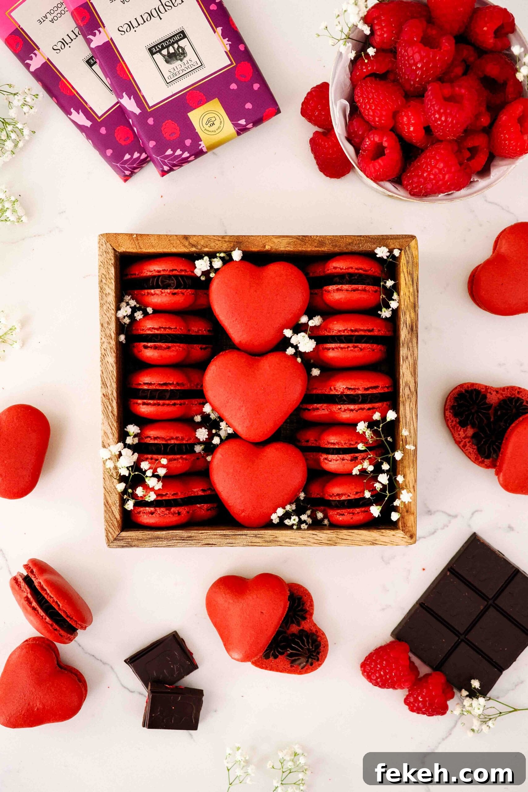 A wooden box is filled with red, heart-shaped macarons and decorated with baby's breath flowers.