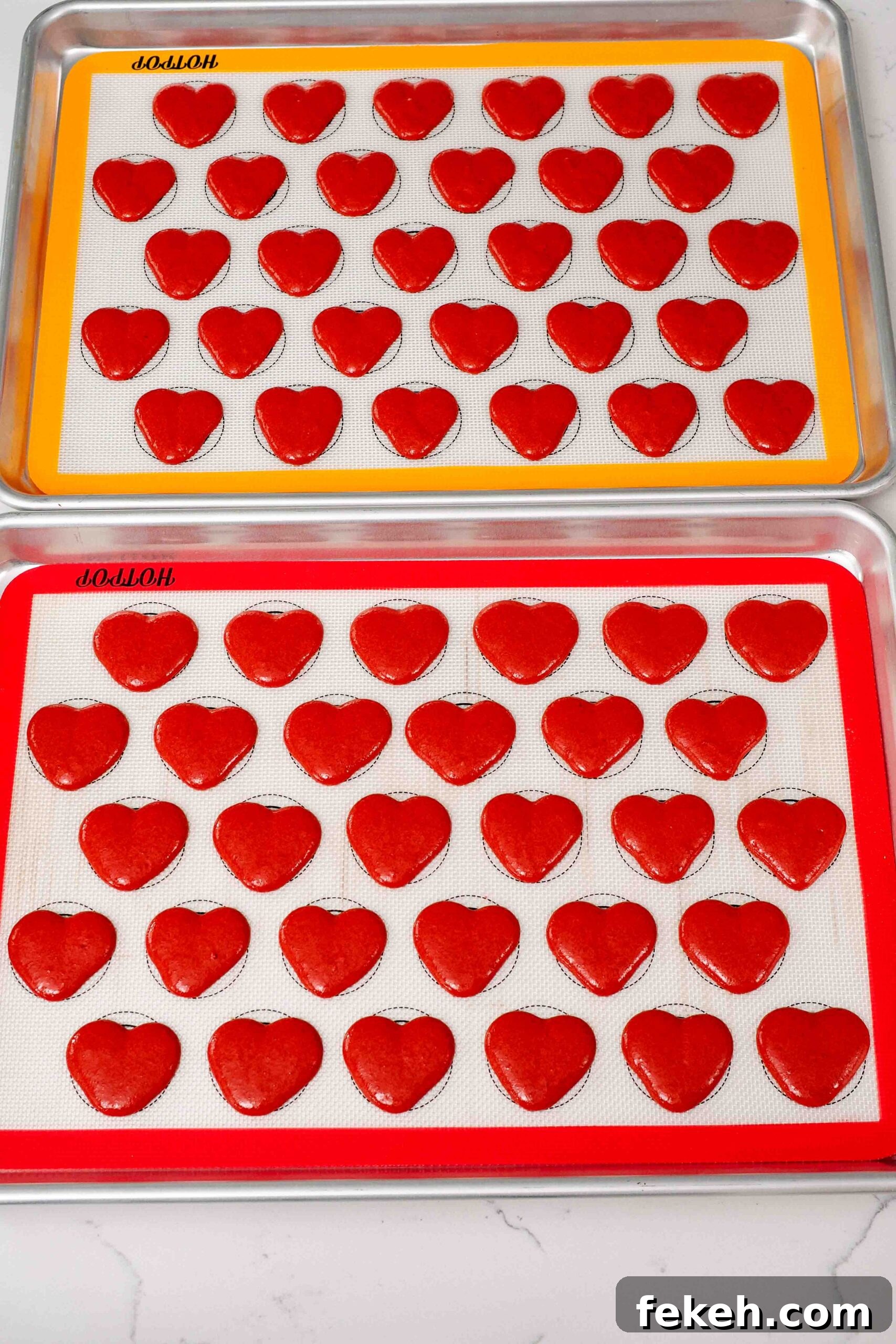Freshly piped heart macarons on silicone macaron mats.