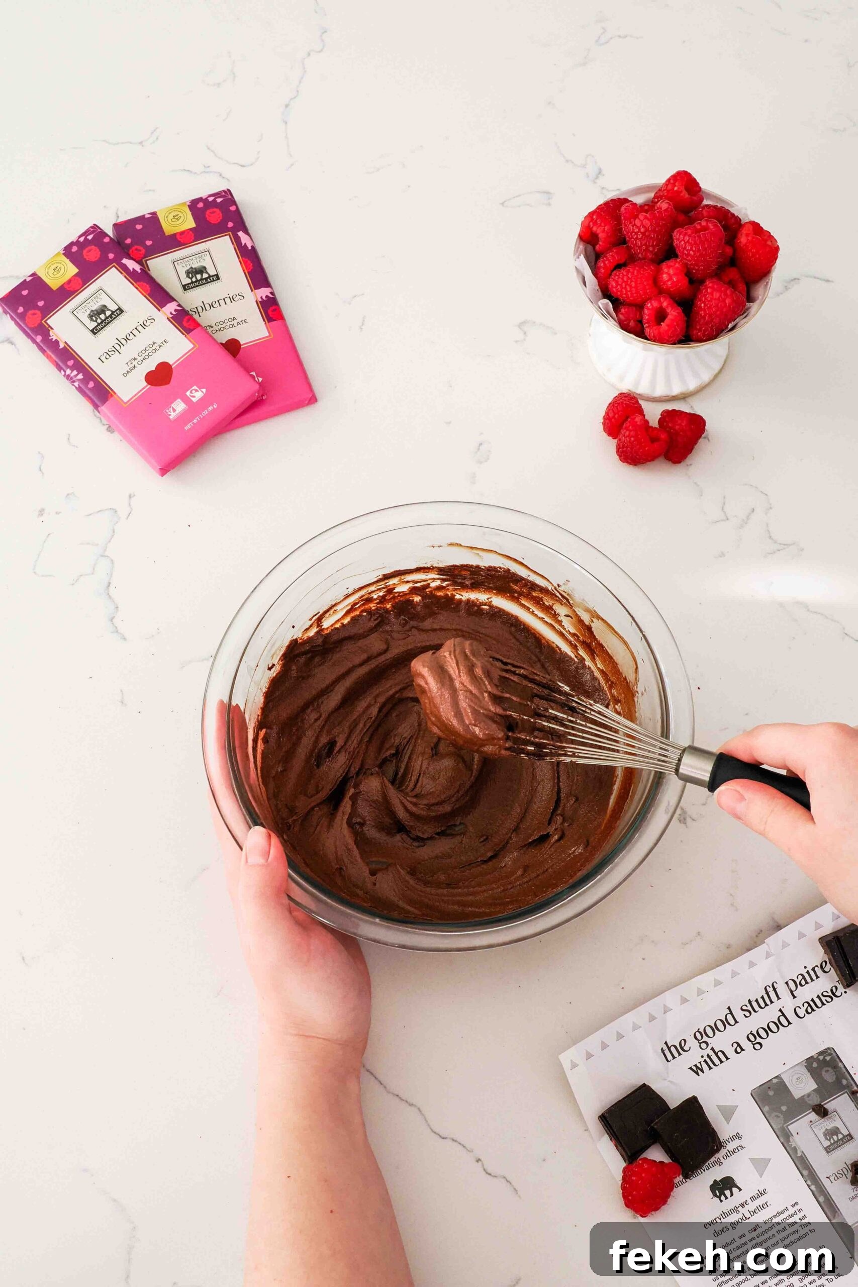 A whisk filled with raspberry chocolate ganache hovers over a bowl of ganache.