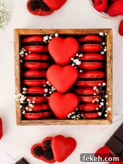 A wooden box is filled with red, heart-shaped macarons and baby's breath flowers.