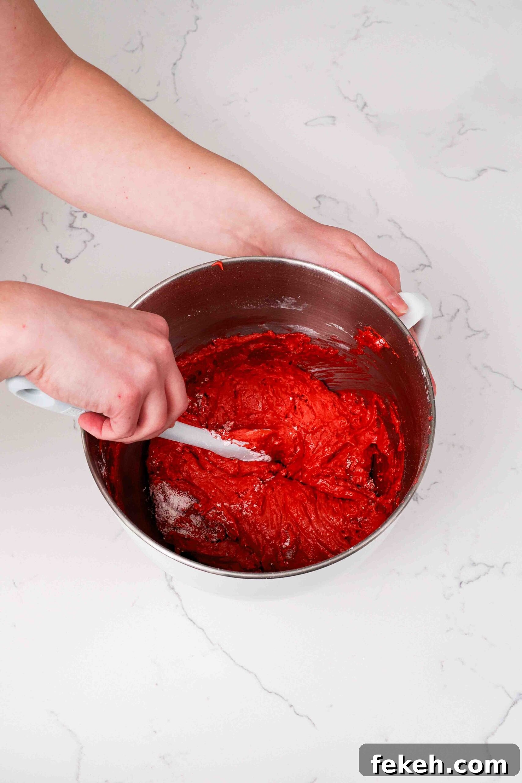Two hands fold macaron batter in a mixing bowl at the early stages, where it's still quite airy.