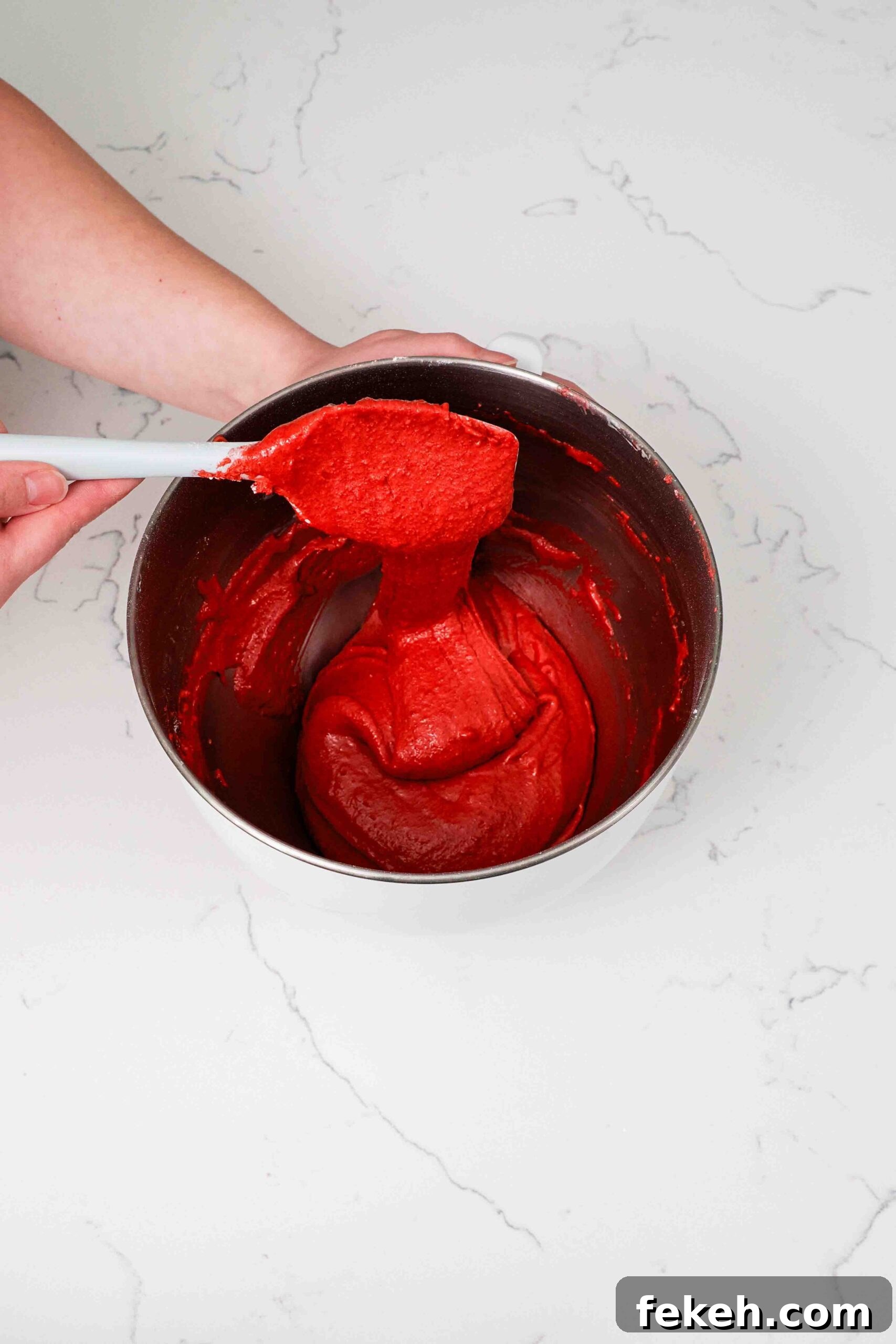 Macaron batter trails off a spatula in a long ribbon.