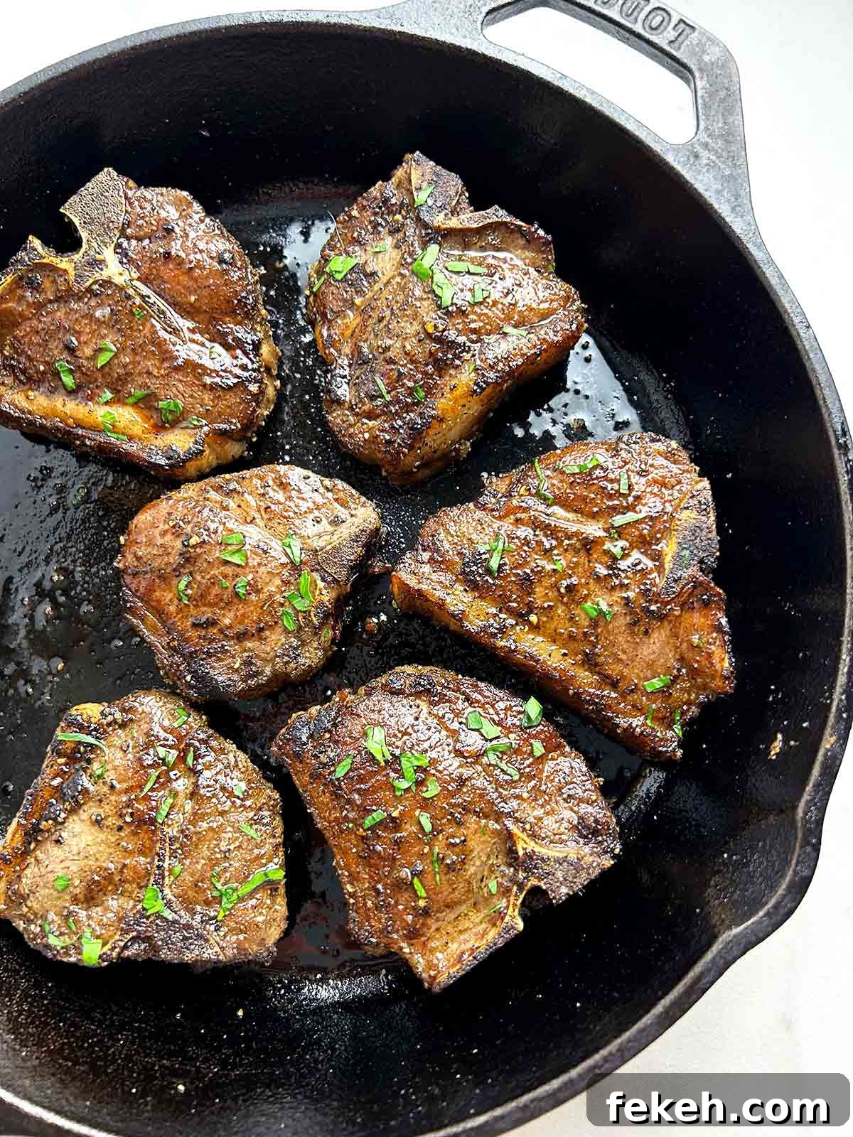 baked lamb loin chops in cast-iron pan with parsley sprinkled on top.