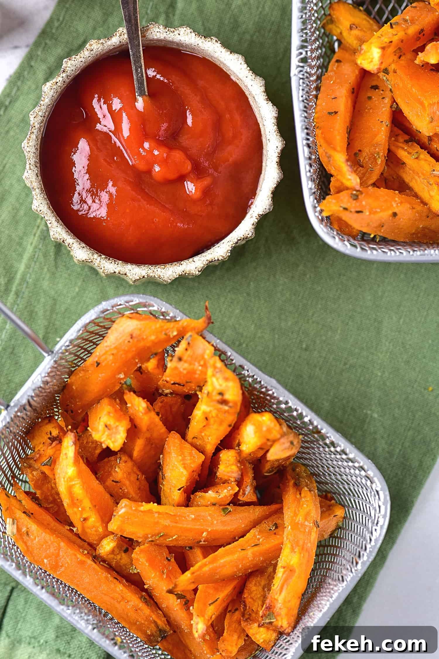 Top down view of sweet potato wedges and ketchup on a green cloth.