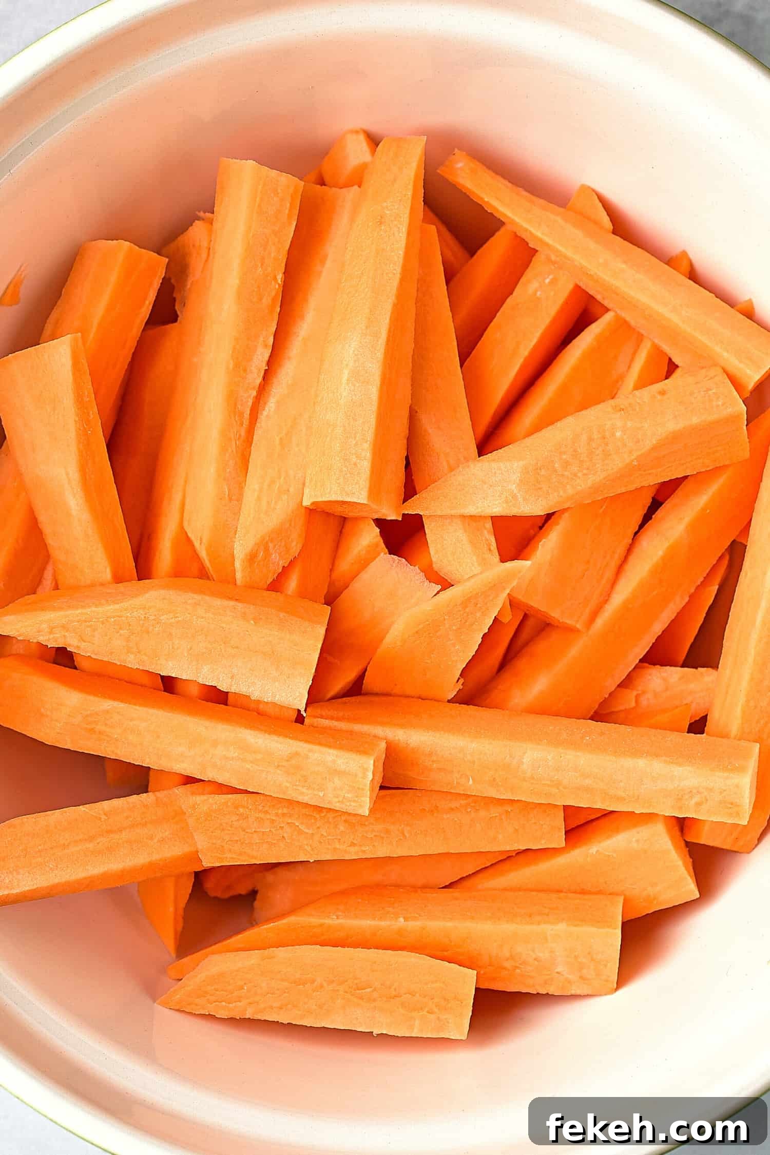 Top down view of uncooked cut sweet potatoes in white bowl.
