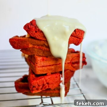 cream cheese glaze poured over top of a stack of red velvet waffles.