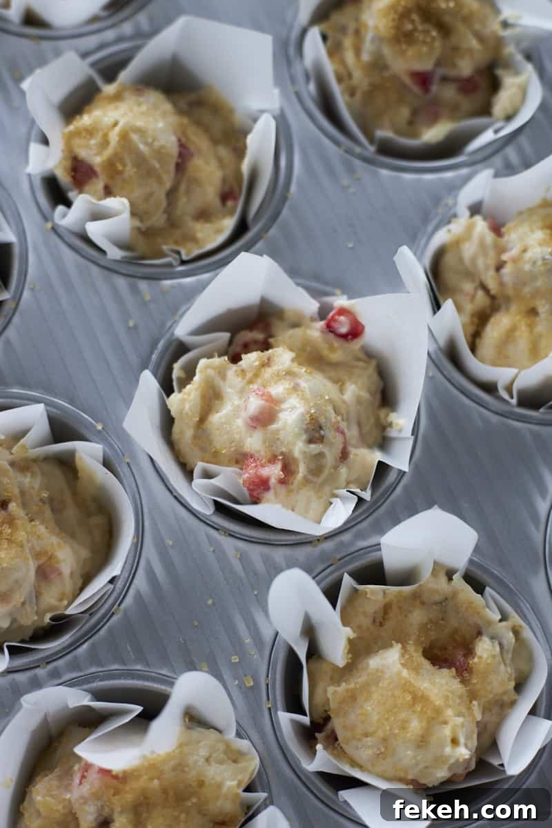 Strawberry Almond Muffins Recipe with Crispy Streusel Topping 10 Batter in white muffin liners in a muffin tin.