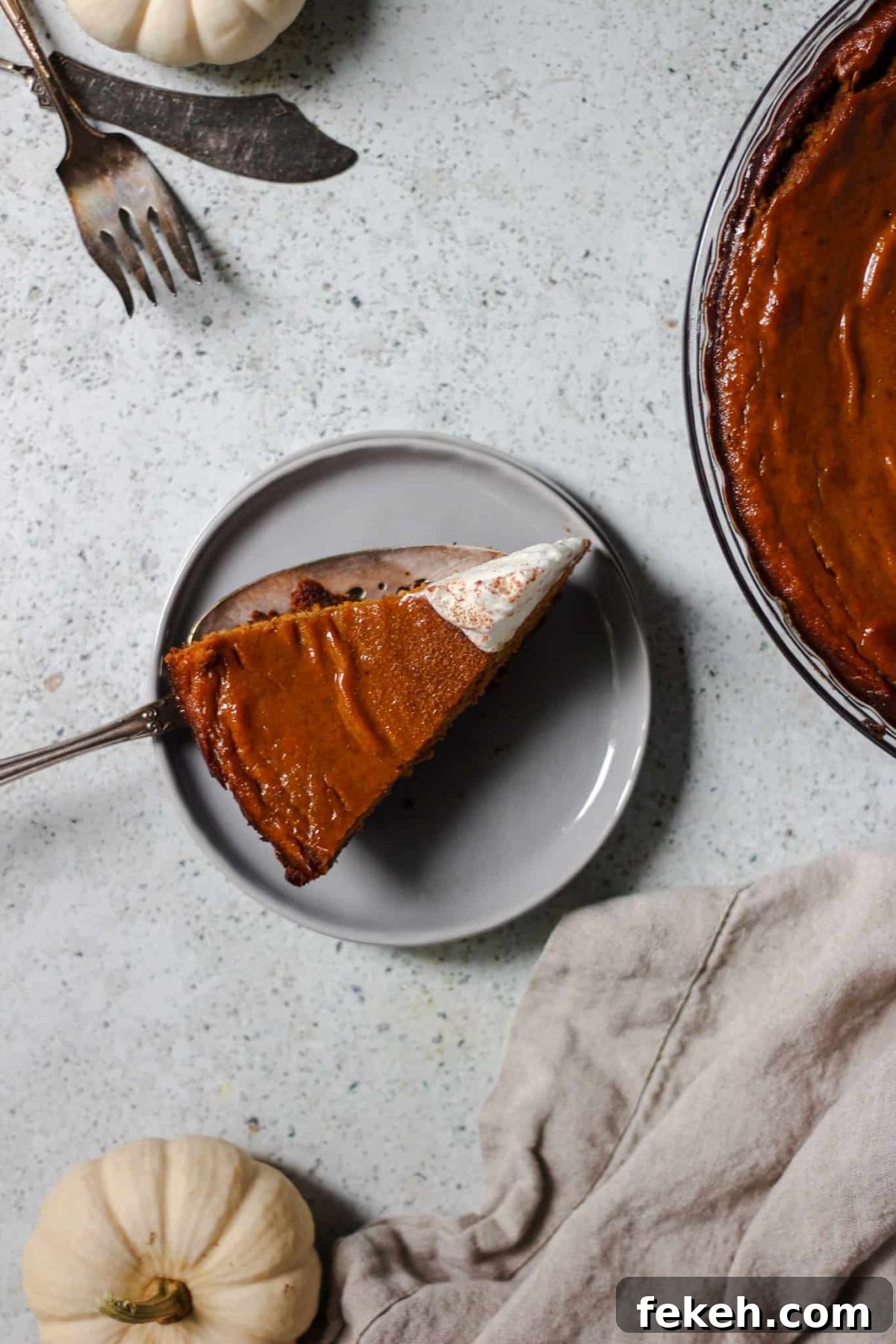flatlay photo of a slice of fall pie with a linen, silverware and a small white pumpkin