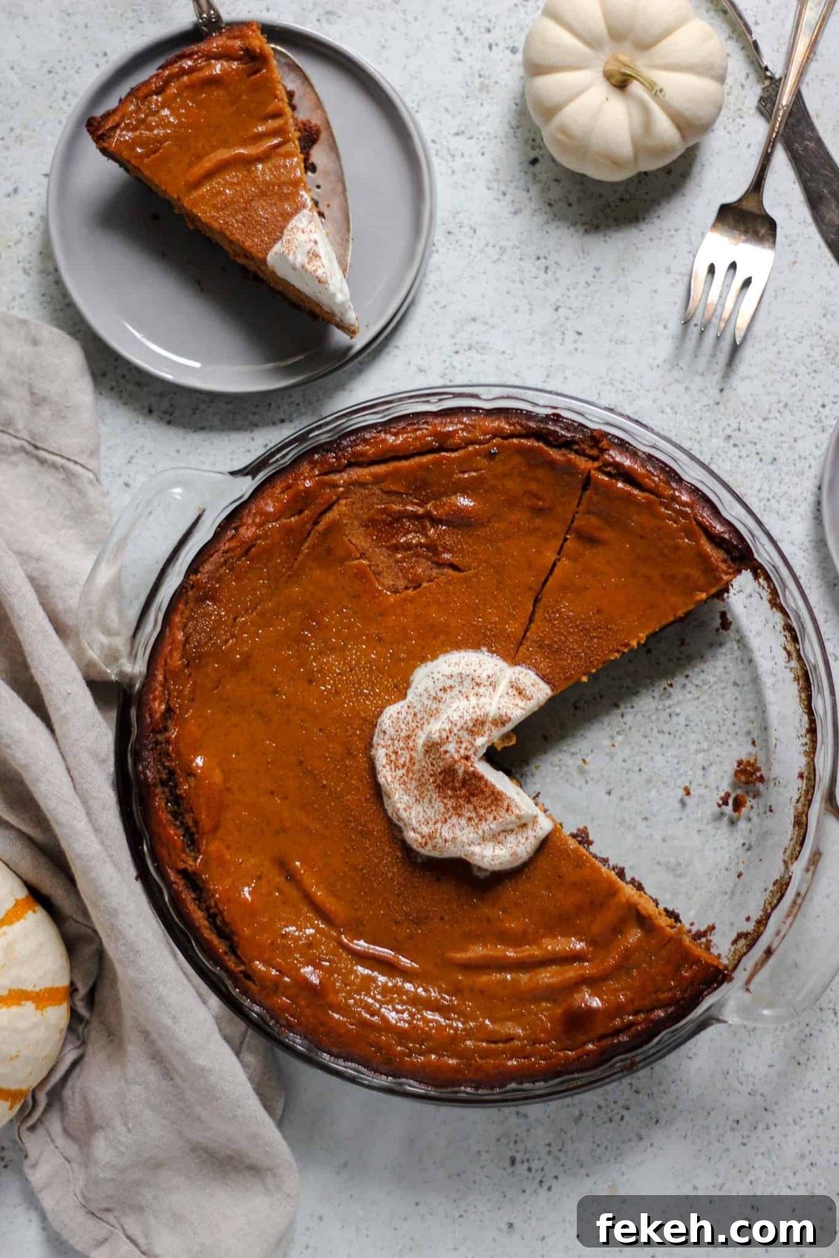 flatlay of pumpkin pie in a round glass dish with a slice of pie on a small grey plate