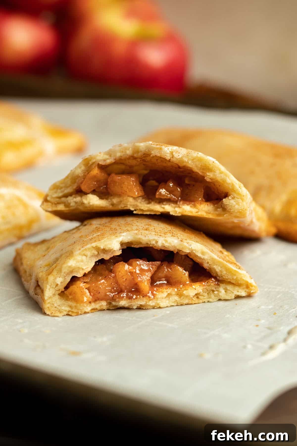 cinnamon apple pop tart cut in half to show the filling while resting on a sheet pan with red apples in the background