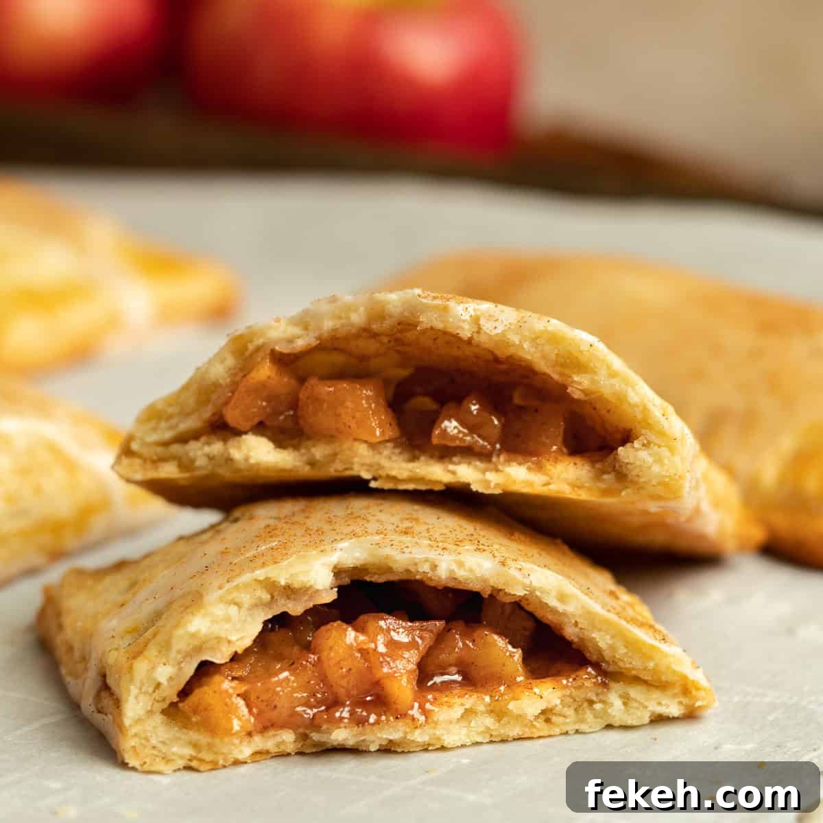 cinnamon apple pop tart cut in half to show the filling while resting on a sheet pan with red apples in the background