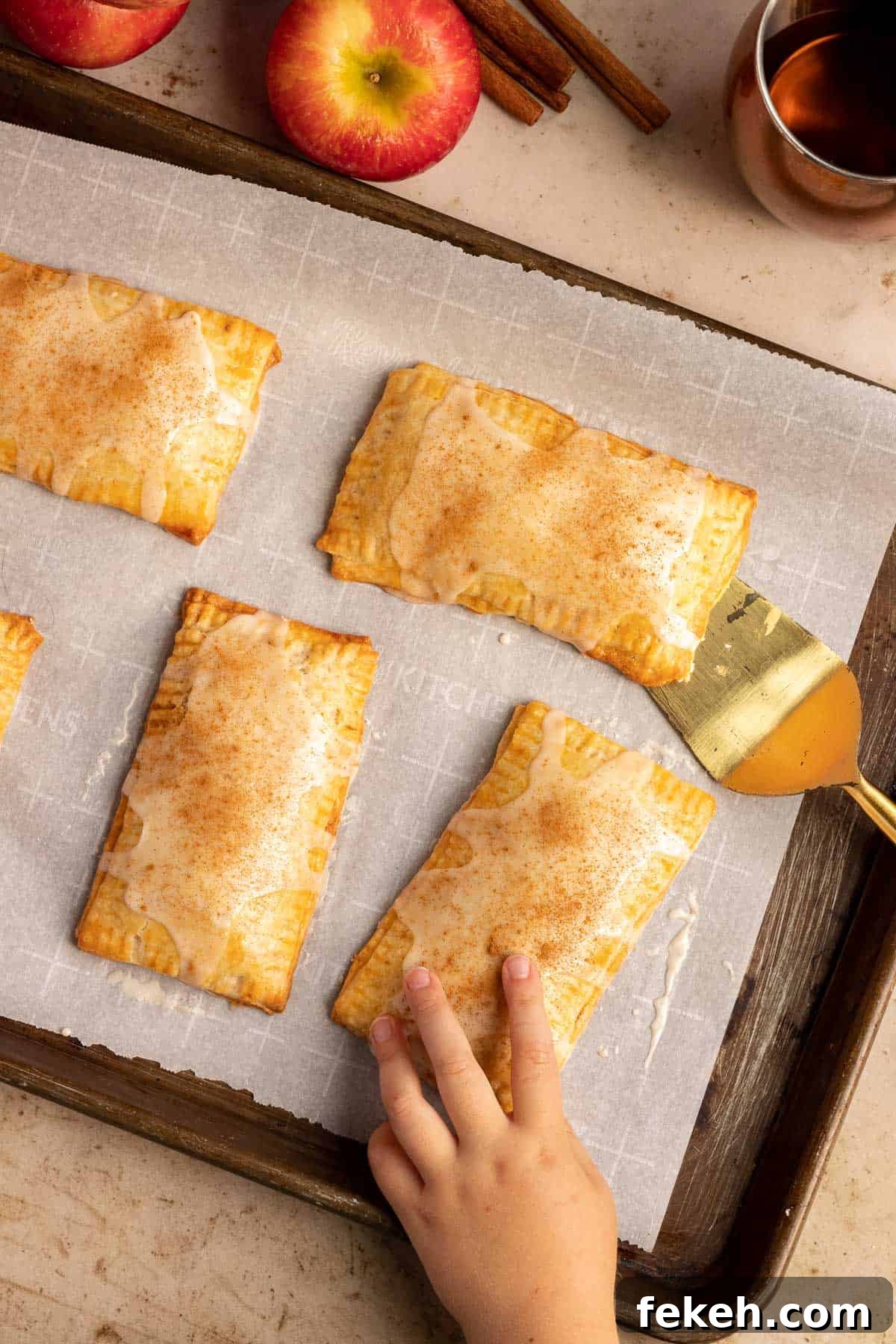 cinnamon apple pop tarts on a baking sheet with a child's hand grabbing one from the sheet