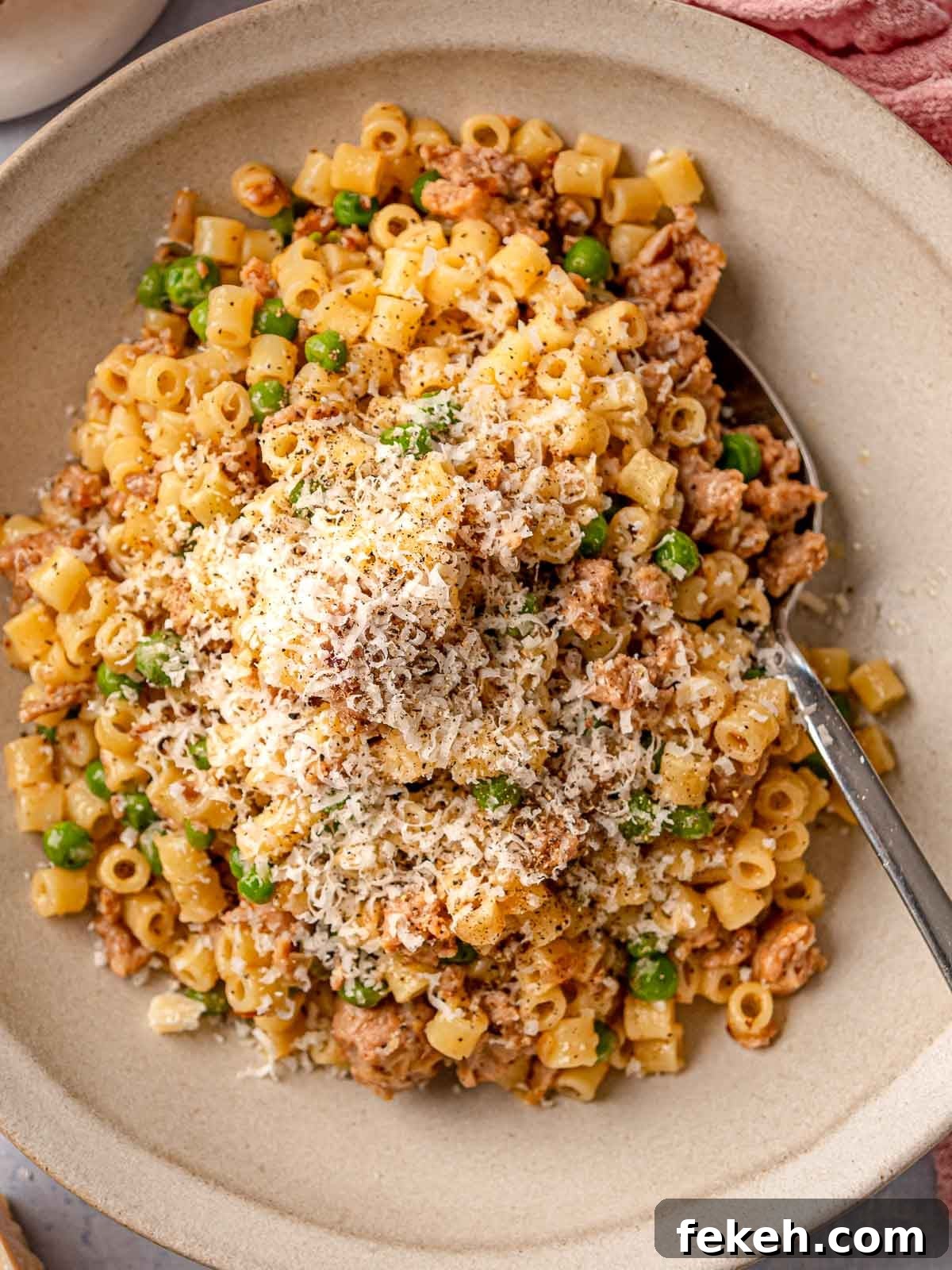 Ditalini Pasta with Italian Sausage and Peas 2 A serving of ditalini with crumbled sausage, peas, and freshly grated Parmesan in a neutral stoneware bowl with a spoon.