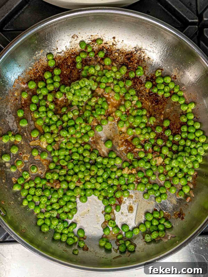 Ditalini Pasta with Italian Sausage and Peas 5 Bright green peas cooking in a stainless steel skillet with browned bits from the sausage.