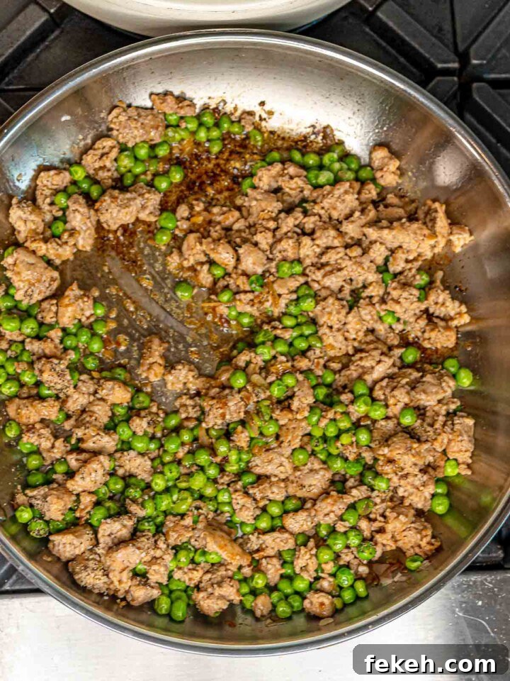 Ditalini Pasta with Italian Sausage and Peas 6 Crumbled sausage and green peas combined in a stainless steel skillet, being stirred with a spatula.