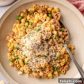 Ditalini Pasta with Italian Sausage and Peas 10 A stoneware bowl filled with ditalini pasta, crumbled sausage, and peas, finished with grated Parmesan and cracked black pepper, with a spoon and pink linen alongside.
