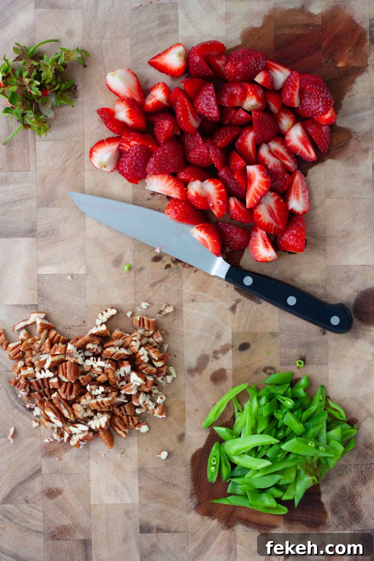 Strawberry Goat Cheese Salad with Balsamic Glaze 4 Strawberries, snap peas and pecans chopped on a wooden cutting board.