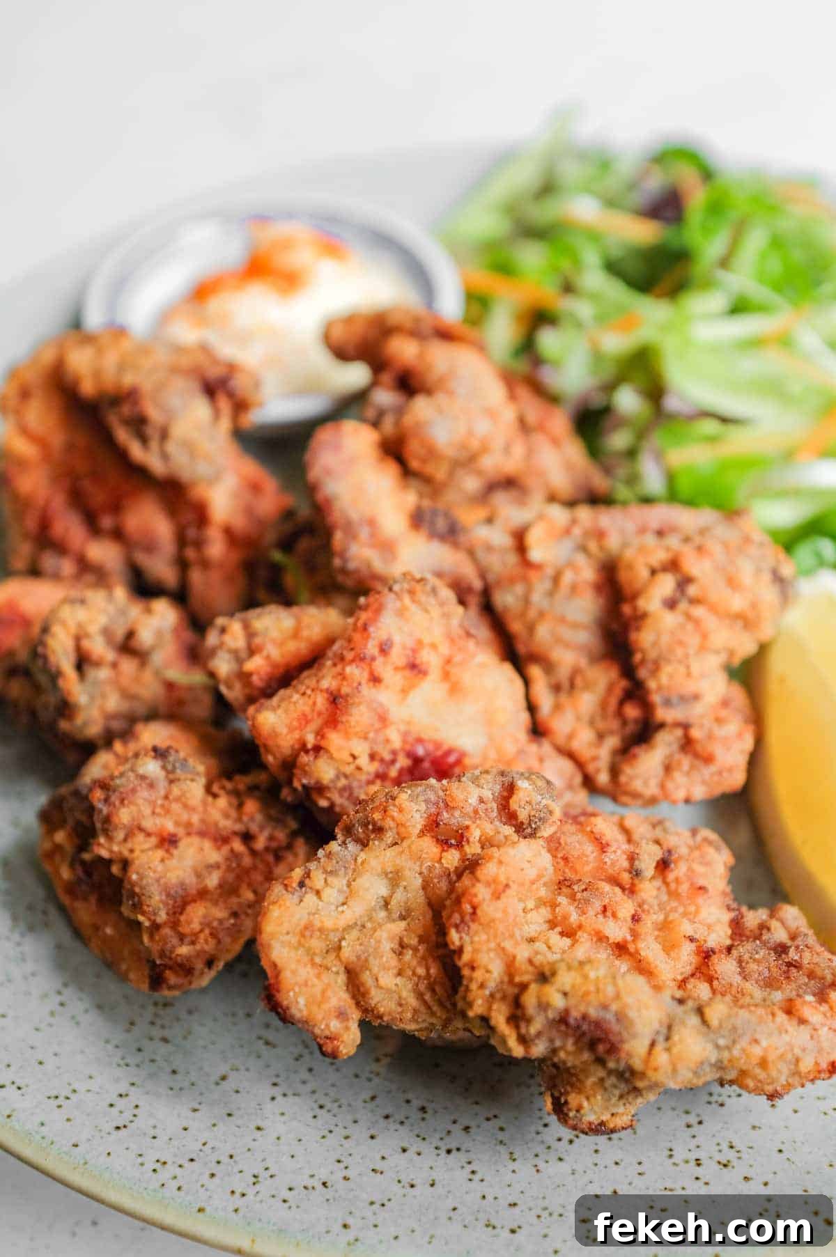 A plate of Japennese karaage chicken with a side salad, lemon wedge, and mayonnaise