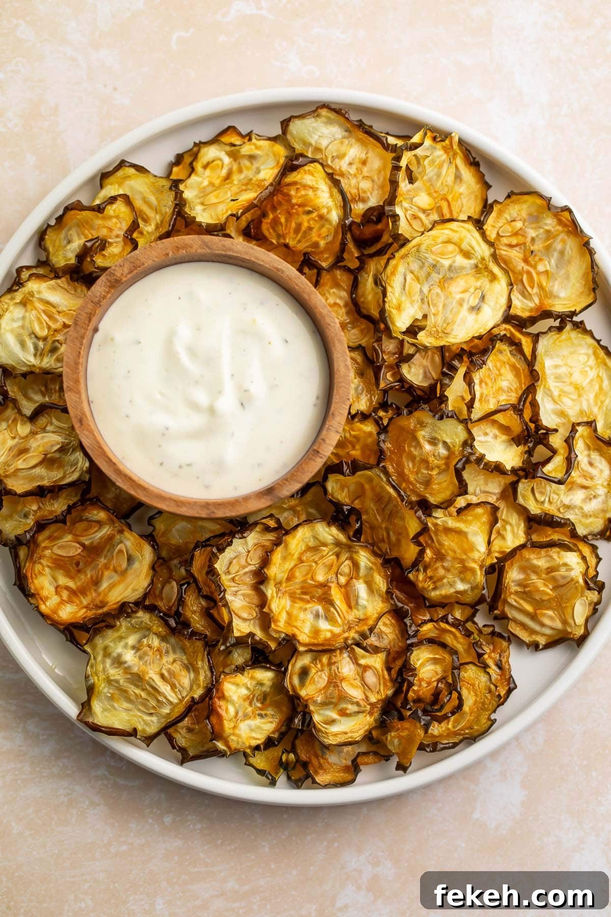 Crispy Baked Cucumber Chips Recipe for Low-Carb Snacking 3 Crispy cucumber chips arranged around a bowl of ranch dressing on a large rimmed plate.