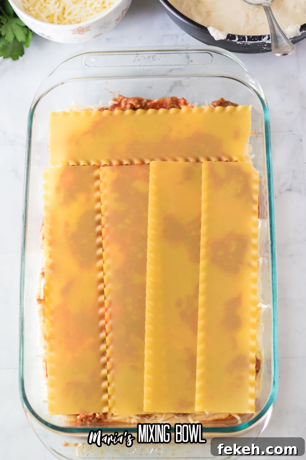 noodles, sauce and cheese being layered in a glass casserole dish