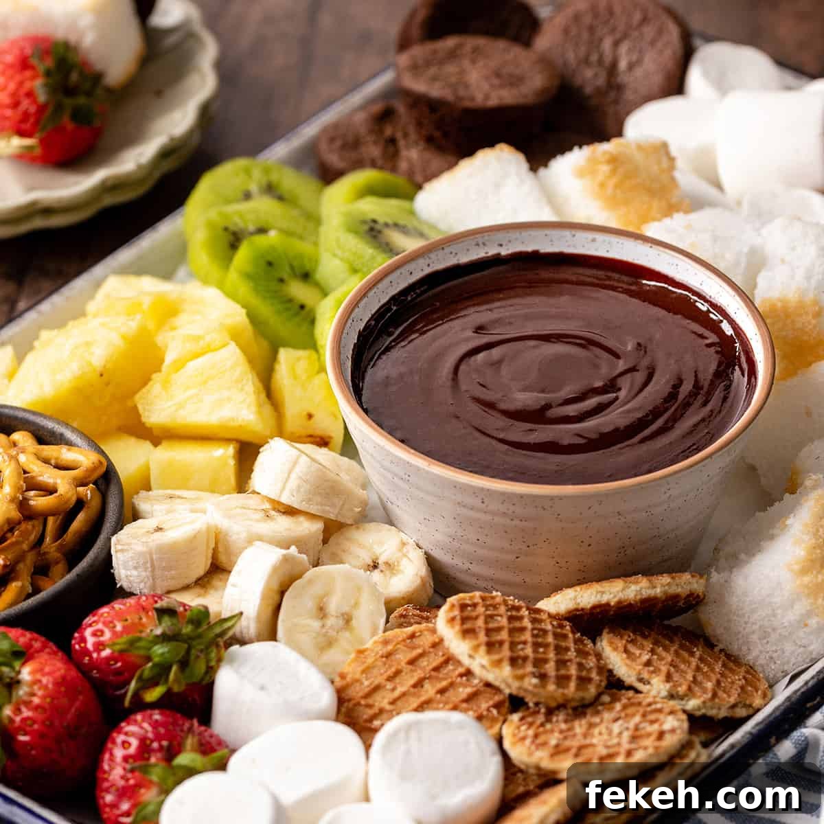 Decadent Chocolate Fondue Recipe for Dipping Fruit & Treats 10 a bowl of Chocolate Fondue surrounded by chocolate fondue dippers like cookies, fruit and cake.
