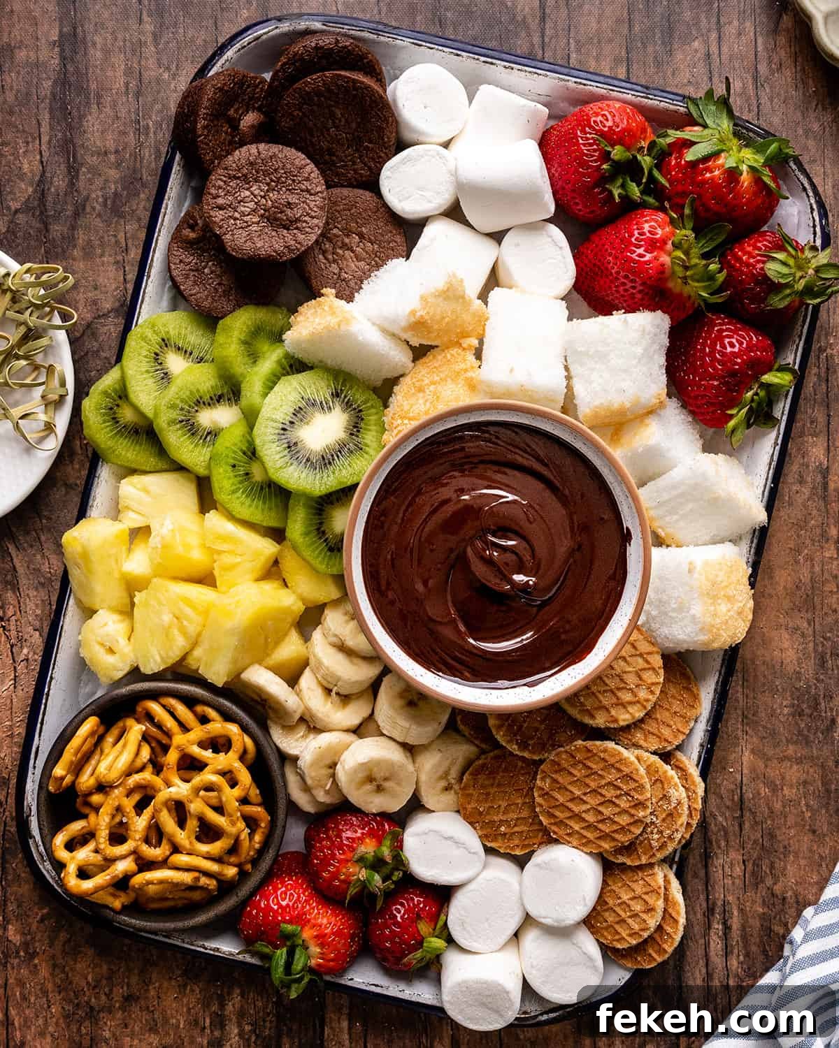 Decadent Chocolate Fondue Recipe for Dipping Fruit & Treats 11 a bowl of Chocolate Fondue surrounded by fruit, cake, brownies, cookies and pretzels