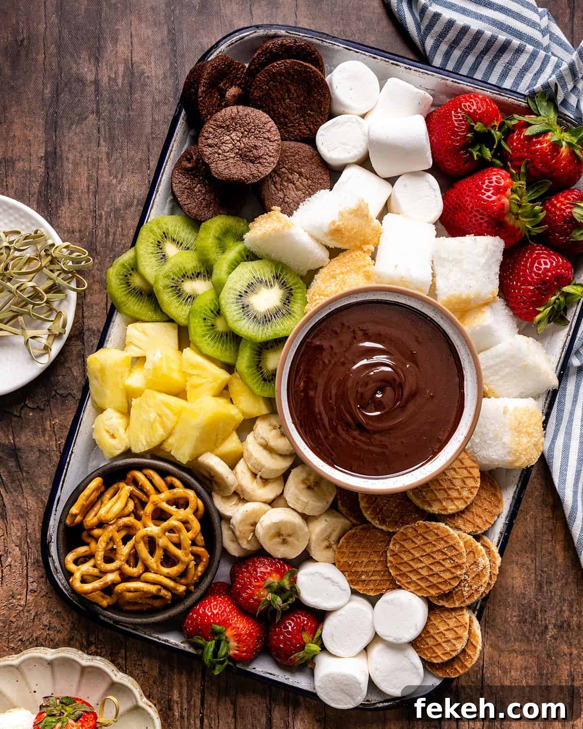 Decadent Chocolate Fondue Recipe for Dipping Fruit & Treats 8 a bowl of Chocolate Fondue surrounded by fruit, cake, brownies, cookies and pretzels