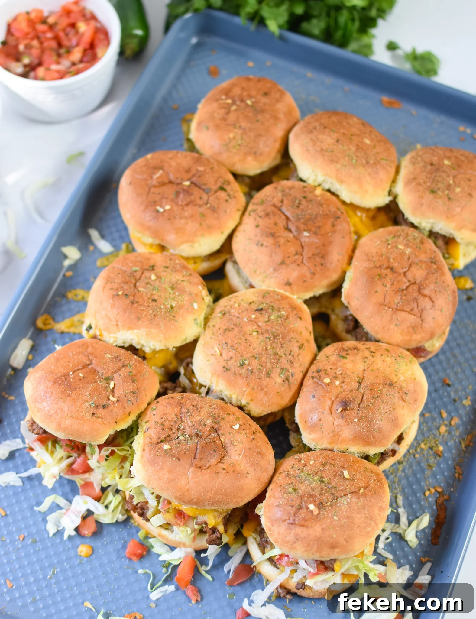 Taco Beef Sliders: Quick Party Sliders with Spicy Beef & Cheese 7 Taco Beef Sliders on a baking sheet with garnishes.