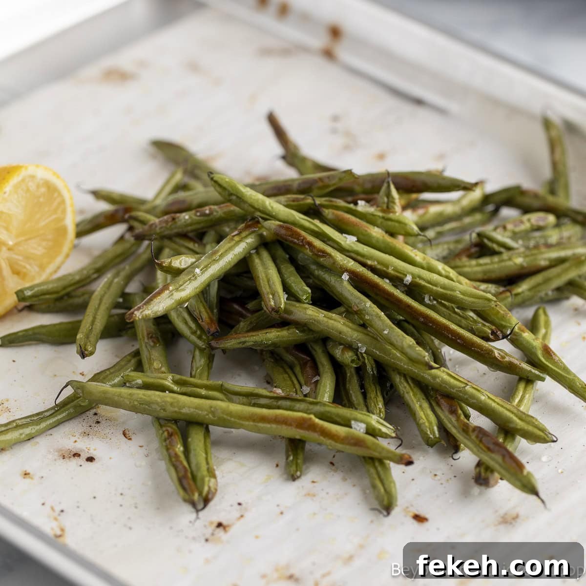 Crispy Oven-Roasted Green Beans with Garlic and Parmesan 6 Roasted beans on a baking sheet with a half of a lemon.