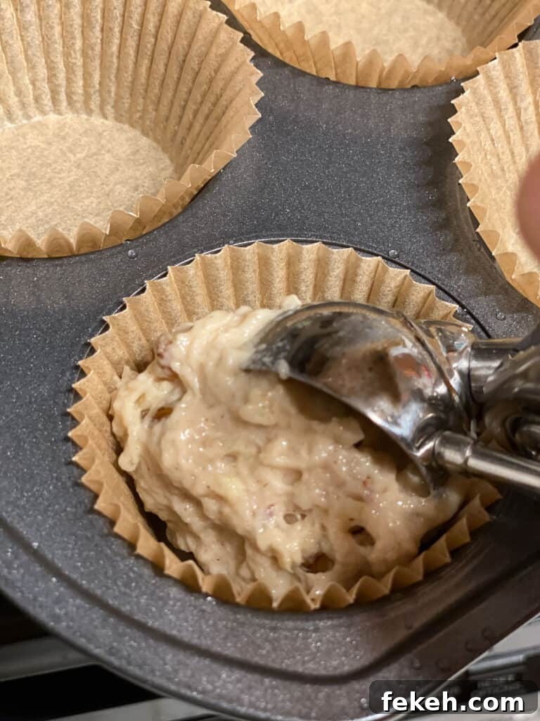 process of adding apple muffin mixture to baking cupcake liner in muffin tray