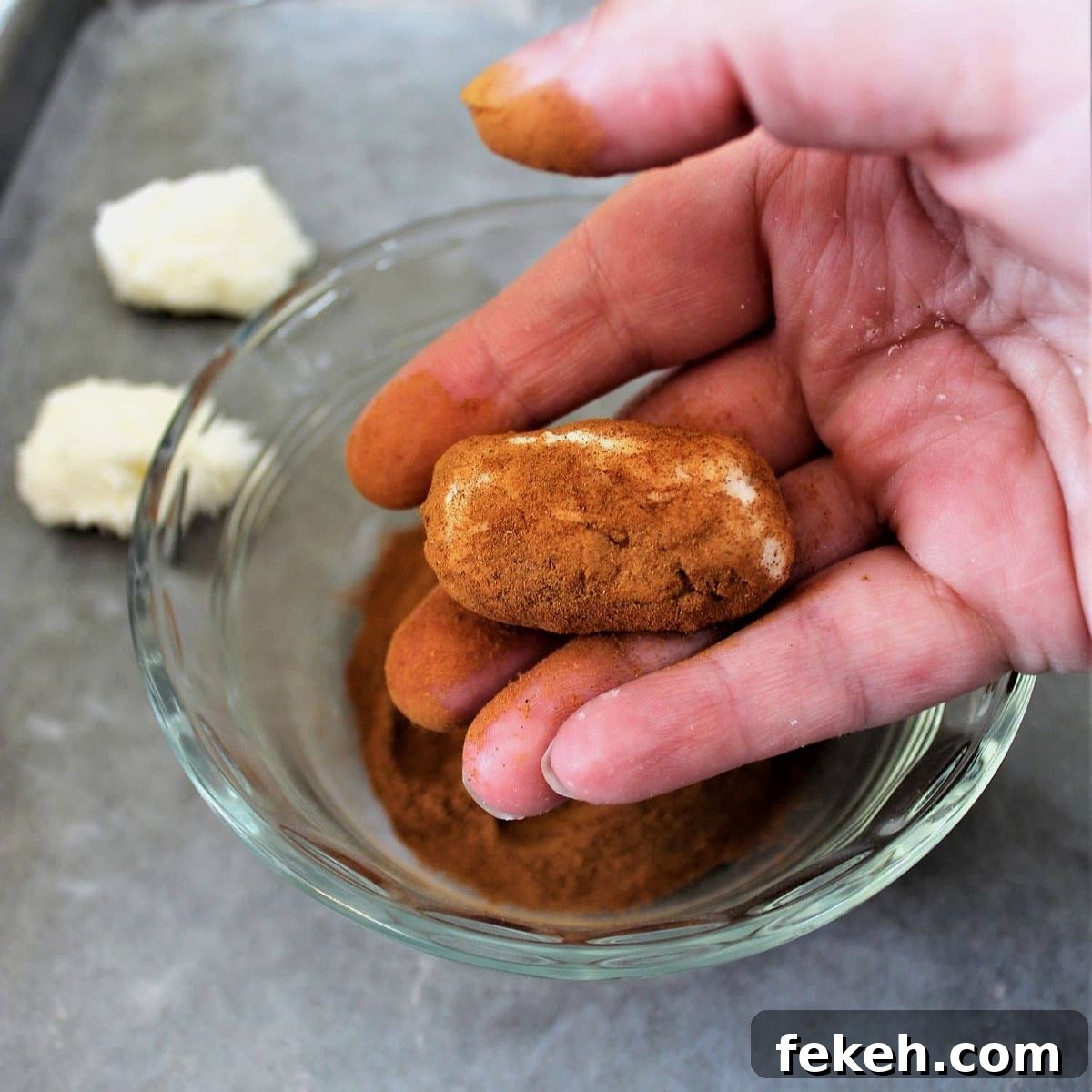 dredging potato-shaped candy in cinnamon mixture in small glass bowl.