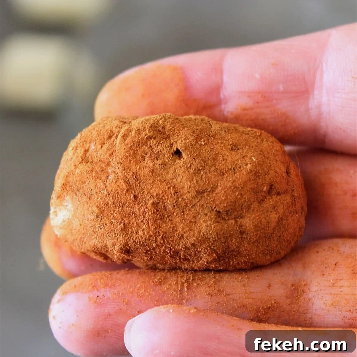 one potato candy in hand all covered in cinnamon.