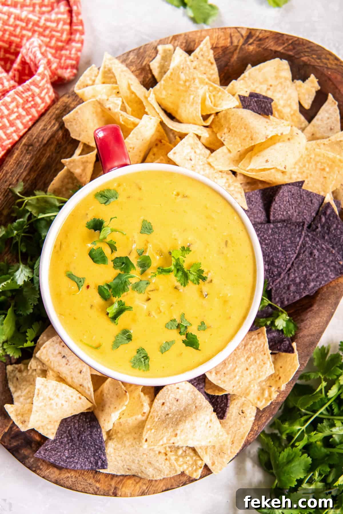 Slow Cooker Chicken Queso Dip Recipe for Game Day Snacks 2 Chicken queso dip in a red-handled bowl on a wood board with blue and white corn chips.