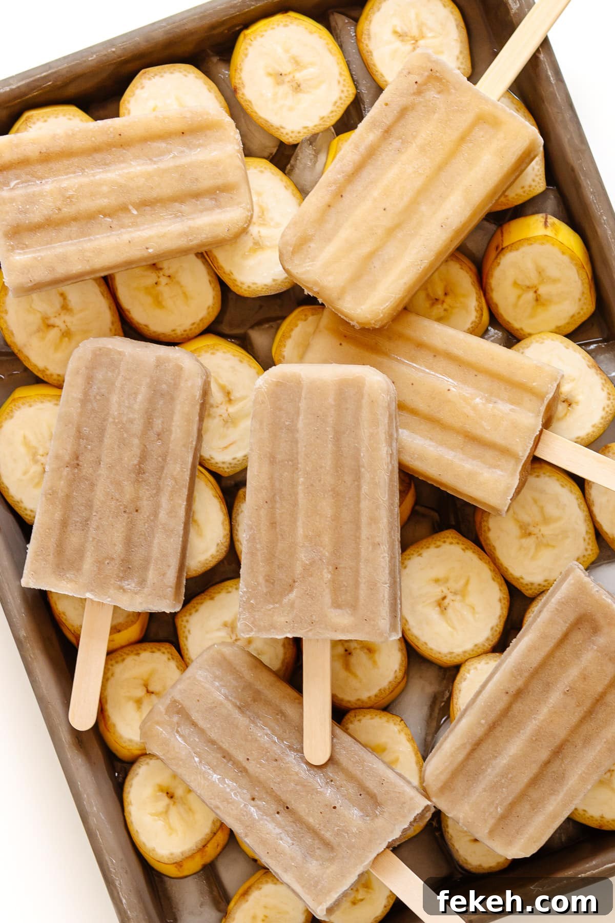 Homemade Banana Popsicles: Creamy No-Sugar Frozen Treats 3 Banana popsicles sitting on a tray of banana slices.