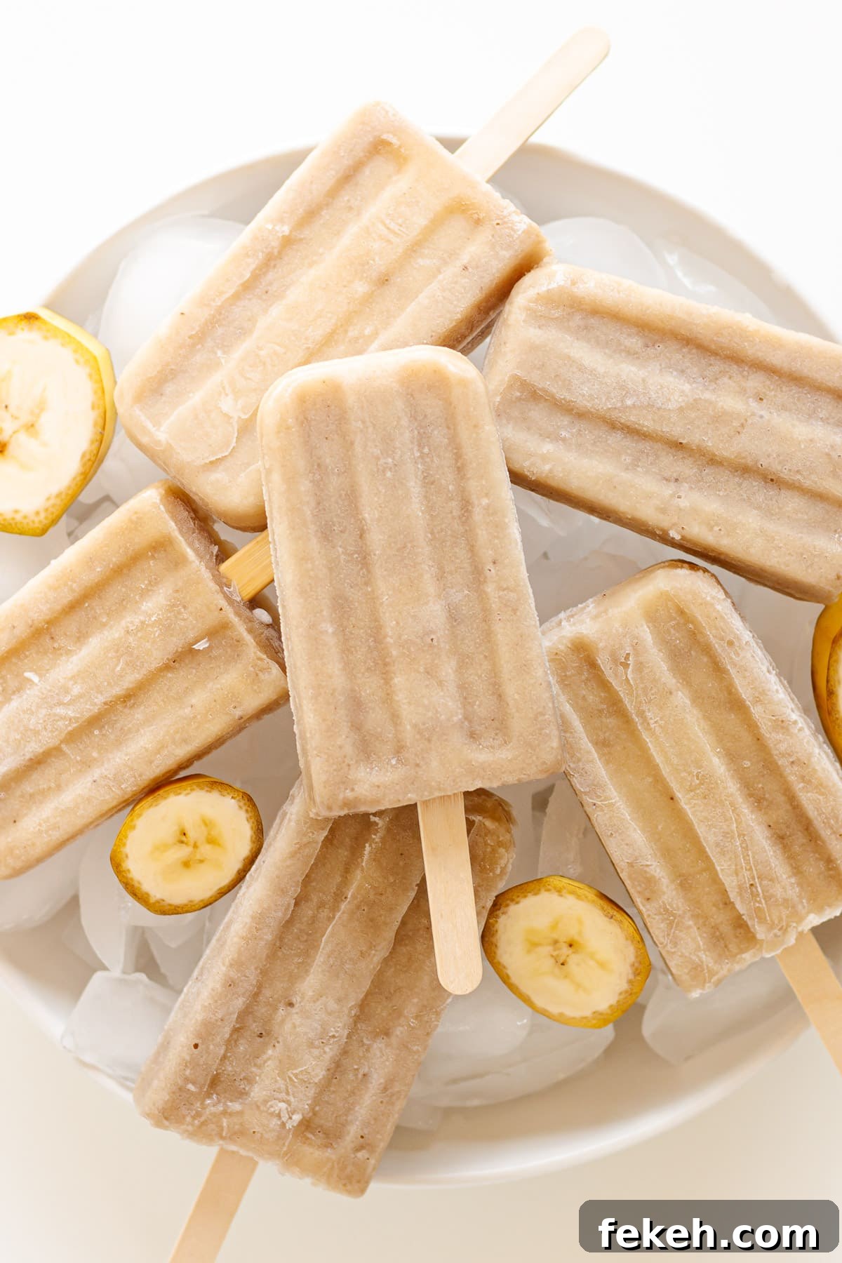 Homemade Banana Popsicles: Creamy No-Sugar Frozen Treats 8 Banana popsicles piled on top of a large white serving bowl of ice.