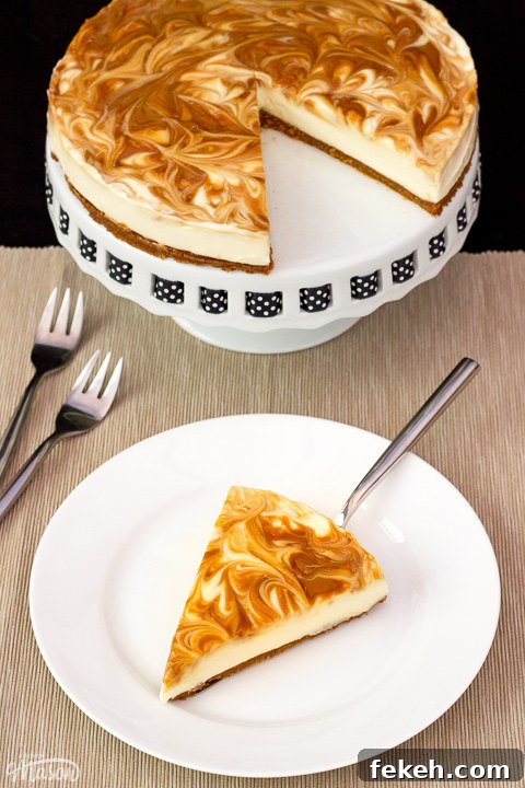 No-Bake Biscoff Cheesecake Recipe with Crunchy Cookie Crust 2 A slice of no bake Biscoff cheesecake on a white plate with a cake slice underneath. The rest of the cheesecake is on a cake stand in the background along with 2 forks.
