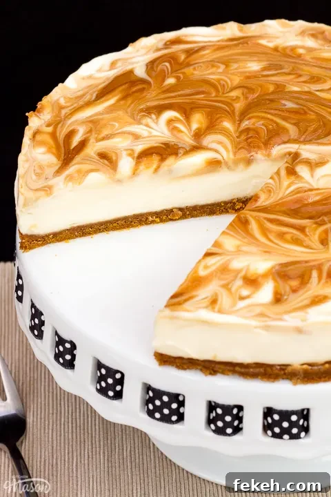 No-Bake Biscoff Cheesecake Recipe with Crunchy Cookie Crust 5 Close up of a Biscoff cheesecake with a slice out of it, set on a cake stand against a black backdrop.