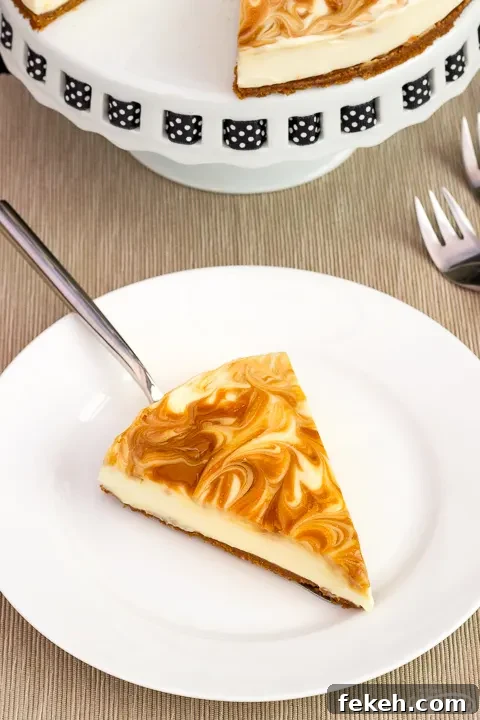 No-Bake Biscoff Cheesecake Recipe with Crunchy Cookie Crust 7 A slice of no bake Biscoff cheesecake on a white plate with a cake slice underneath. The rest of the cheesecake is on a cake stand in the background along with 2 forks.