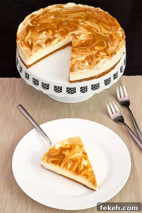 No-Bake Biscoff Cheesecake Recipe with Crunchy Cookie Crust 14 A slice of no bake Biscoff cheesecake on a white plate with a cake slice underneath. The rest of the cheesecake is on a cake stand in the background along with 2 forks.