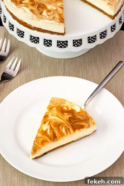 No-Bake Biscoff Cheesecake Recipe with Crunchy Cookie Crust 16 A slice of no bake Biscoff cheesecake on a white plate with a cake slice underneath. The rest of the cheesecake is on a cake stand in the background along with 2 forks.