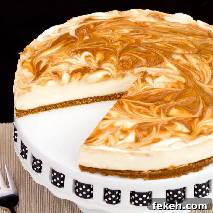 Close up of a Biscoff cheesecake with a slice out of it, set on a cake stand against a black backdrop.