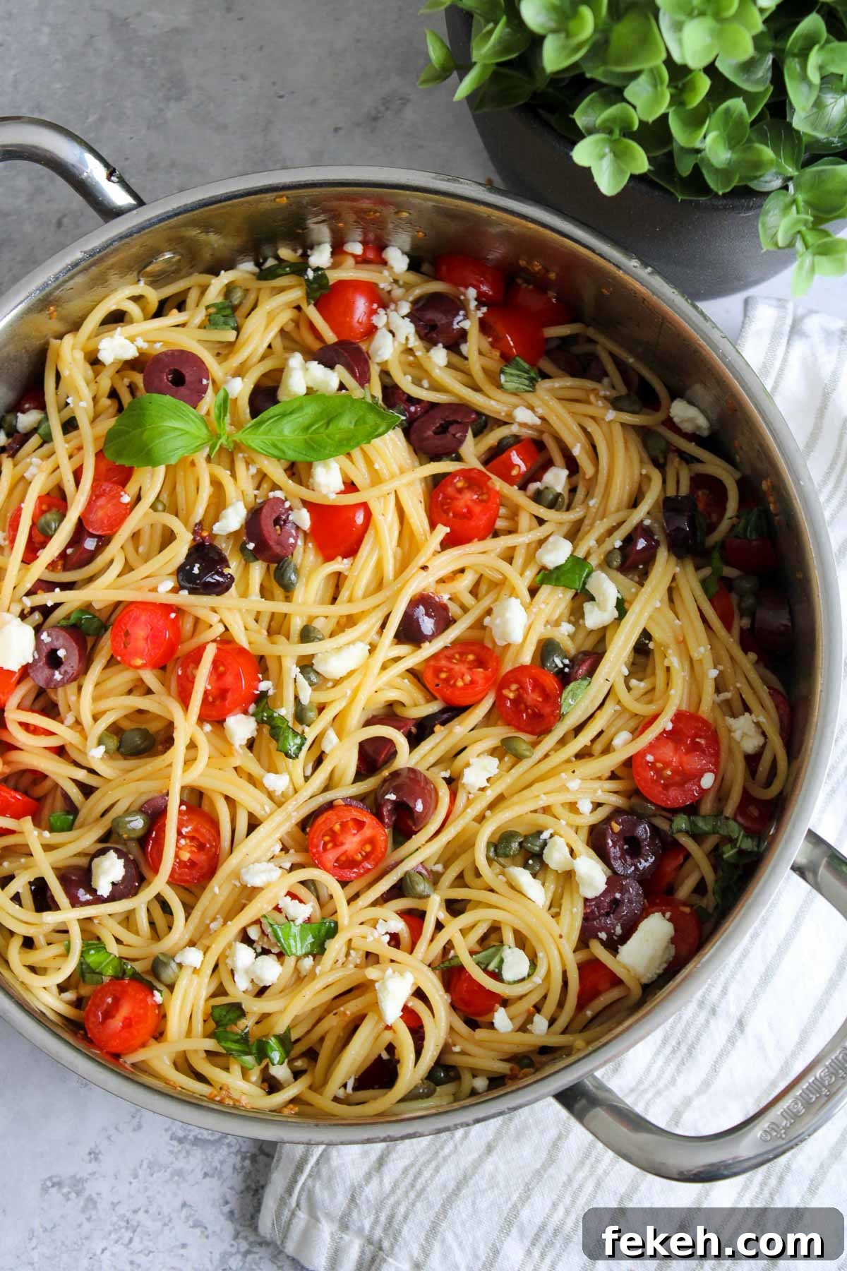 Stove top pot of spaghetti with tomatoes, kalamata olives, feta cheese, and basil mixed all together. 