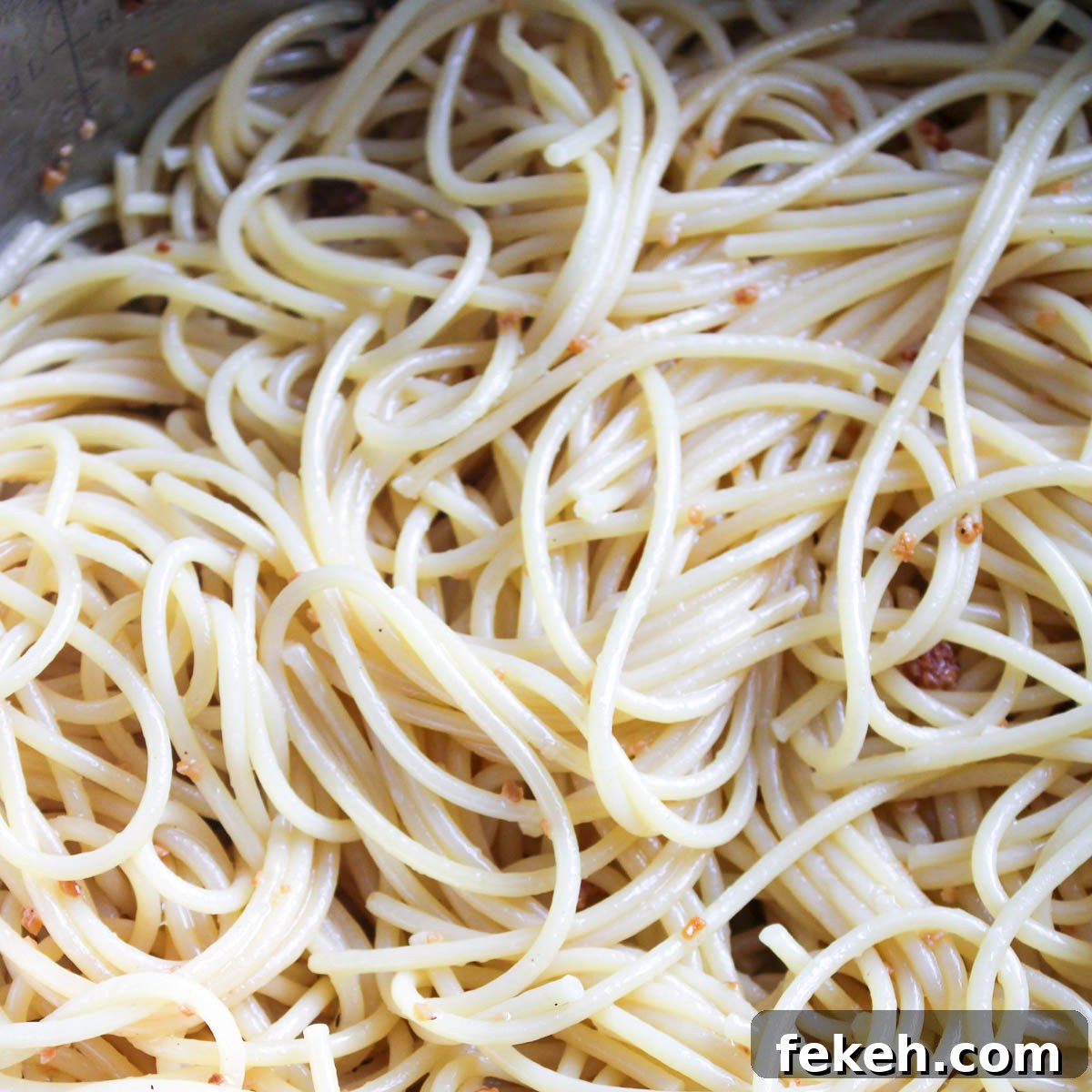 Cooked spaghetti noodles in a pot mixed with the sautéed garlic and olive oil.