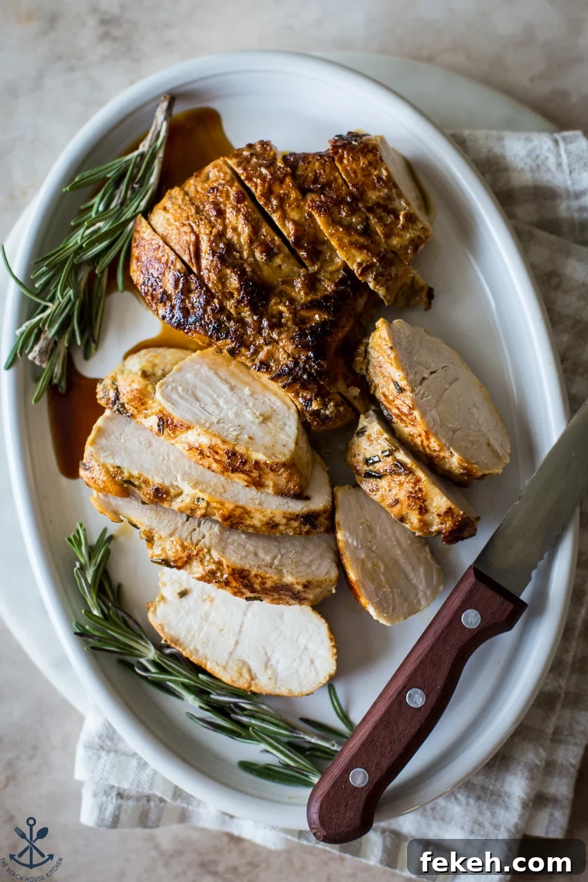 Overhead photo of a sliced turkey tenderloin on an oval plate with two sprigs of rosemary and a sharp knife