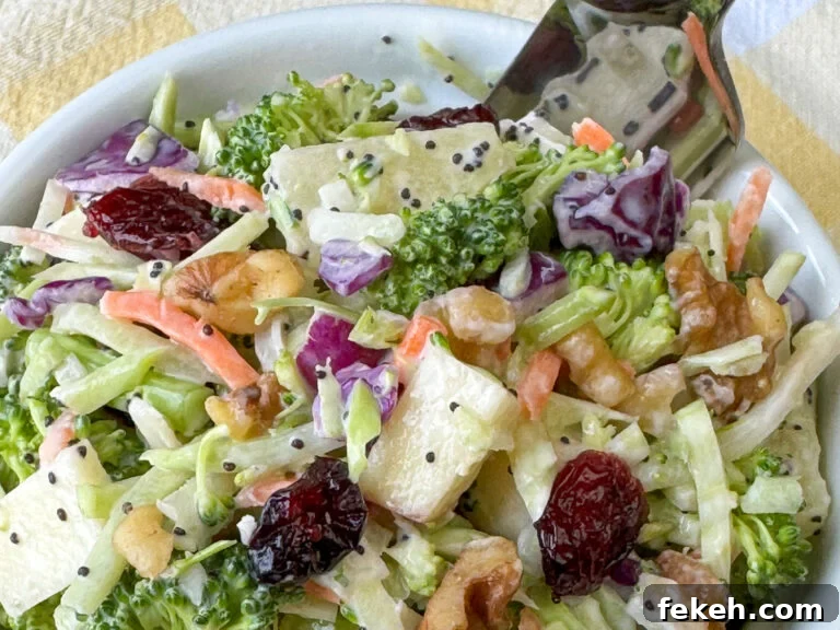 Creamy Broccoli Slaw with Crunchy Apples and Almonds 2 Overhead view of a small dish of broccoli slaw salad with a simple creamy dressing and a fork on a yellow and white plaid napkin.